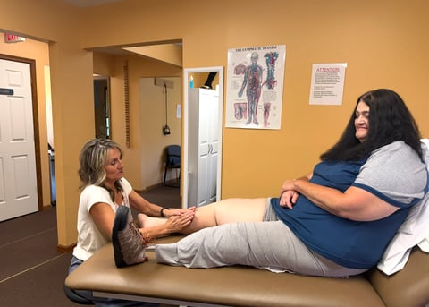 Physical therapist examining patients leg in a medical clinic with yellow walls and anatomical charts