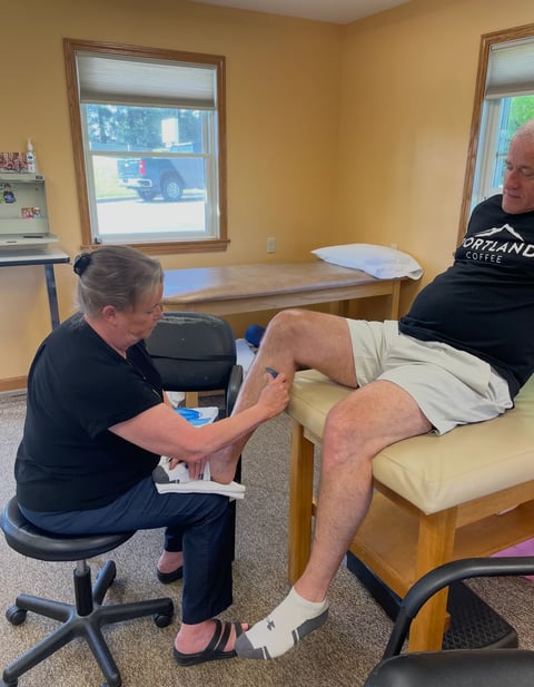 Physical therapist performing leg examination on patient lying on medical table in treatment room