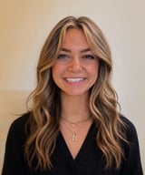 Smiling young woman with blonde wavy hair wearing a white blouse, photographed outdoors with a blurred background