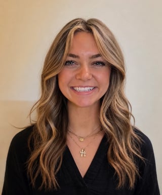 Smiling young woman with blonde wavy hair wearing a white blouse, photographed outdoors with a blurred background