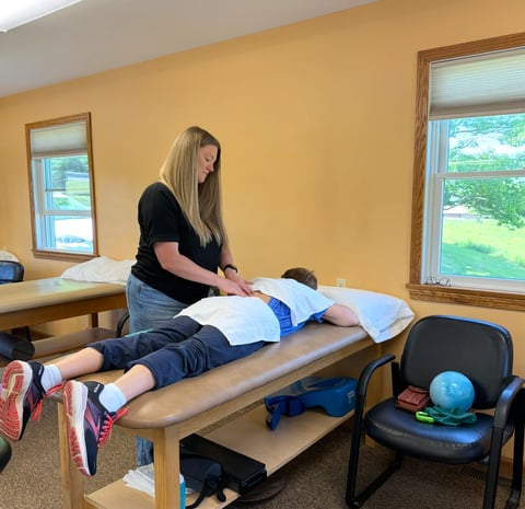 Physical therapist performing spinal adjustment on young patient lying on treatment table in bright clinic room